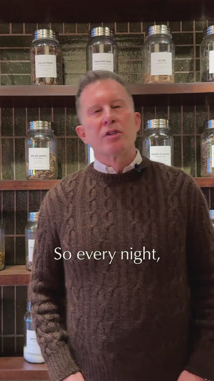 Practitioner speaking in front of TCM apothecary shelving explaining nightly wellness ritual
